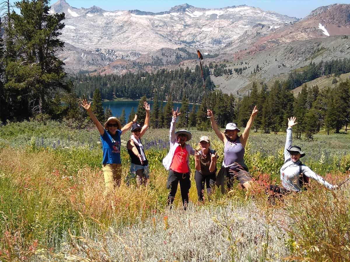 backpacking crew in a field with hands raised