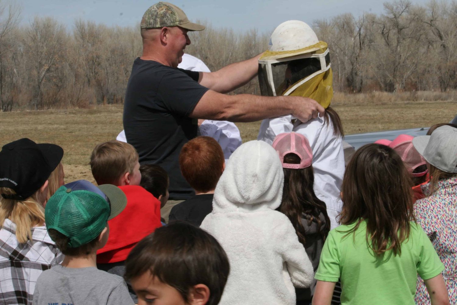 students watching a teacher put on a beekeeper suit